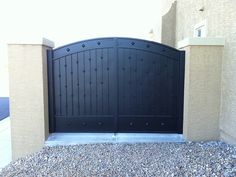 a large black gate is in front of a building with rocks and gravel on the ground