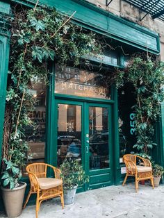 two wicker chairs sitting in front of a green building with ivy growing on it