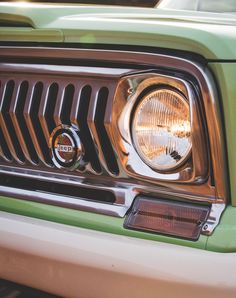 the front end of a green jeep with its lights on and grill grilles down