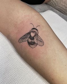 a small black and white bee tattoo on the right upper arm, with heart in it's chest