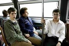 three young men sitting on a bus with their backs to each other and looking at the camera