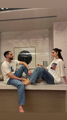 a man and woman sitting on top of a counter next to each other in front of a mirror