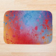 a bath mat with colorful paint splattered on the surface and wood flooring