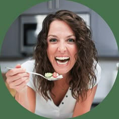 a woman is smiling while holding a spoon with food on it in front of her face