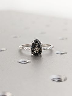 a black diamond ring sitting on top of a silver surface with drops of water around it