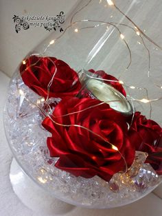 a glass vase filled with red roses on top of a white tablecloth and lights