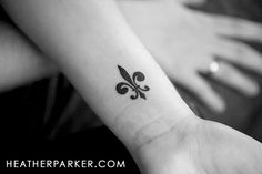 a small black fleur de lis tattoo on the wrist