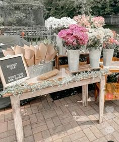 flowers are on display in buckets at an outdoor flower shop with a chalkboard sign