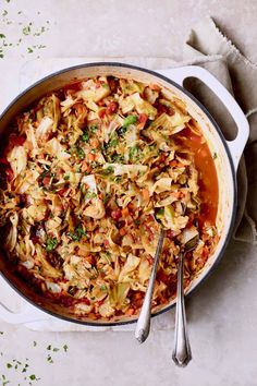 a large pot filled with cabbage and other vegetables next to two spoons on a table