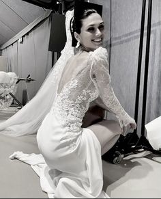 a woman sitting on top of a bed next to a white wall wearing a wedding dress