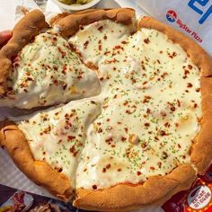 a person is holding a large pizza with cheese and toppings on it, in front of some chips