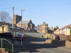 cars are parked on the street in front of some old brick buildings and fenced in area