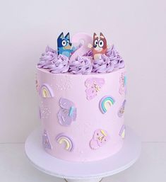 there is a pink cake with purple frosting and two cartoon figures on the top