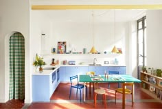 a kitchen with blue and yellow chairs, an island table and shelves on the wall