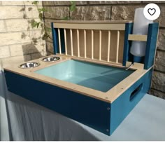 a blue dog bed with two bowls in it and a water dispenser next to it