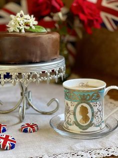 there is a cup and saucer on the table next to a cake with flowers