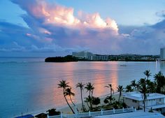 the sun is setting over an ocean with palm trees and buildings in the foreground