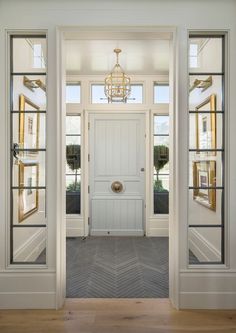 an open door leading into a white room with two windows and a chandelier hanging from the ceiling