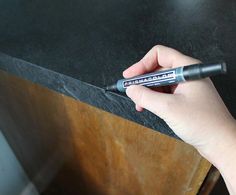 a hand holding a pen on top of a wooden table next to a black counter