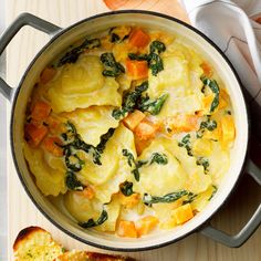 a pot filled with ravioli and spinach on top of a wooden cutting board