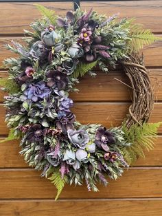 a wreath with purple flowers and greenery hanging on a wooden wall next to a door