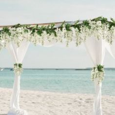 an outdoor wedding setup on the beach with white flowers and greenery draped over it