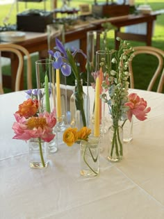 several vases filled with flowers on top of a white table cloth covered tablecloth