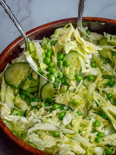 a wooden bowl filled with cucumbers, peas and coleslaw on top of a table