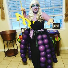 a woman dressed up as a witch holding a wand and balloons in front of her face