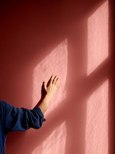 a man standing in front of a pink wall holding his hand out to the side