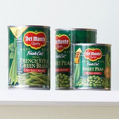 two cans of canned green beans on a shelf next to another can of canned peas