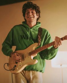 a young man in a green hoodie playing an electric guitar and singing into a microphone