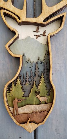 a wooden deer head hanging on the side of a door with trees and mountains in the background