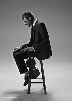 a man sitting on top of a chair with a violin in his lap and wearing a suit