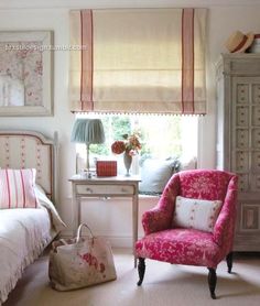 a pink chair sitting in front of a window next to a white bed and dresser