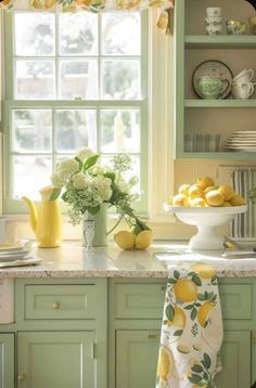 a kitchen with green cabinets and yellow flowers in vases on the window sill