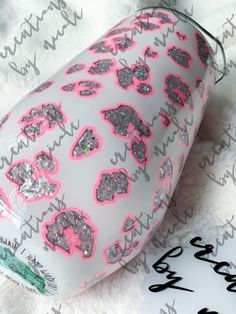 a cup with pink and silver hearts on it sitting on a white blanket next to a name tag