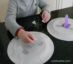 a young boy is making paper plates that look like letters with scissors and glue on them