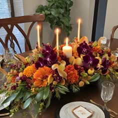 an arrangement of flowers and candles on a dining room table with place settings for dinner