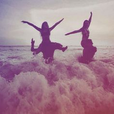 two women are in the ocean with their arms up and one is holding her hands out