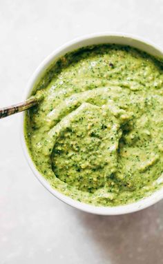 a white bowl filled with pesto sauce on top of a table next to a wooden spoon