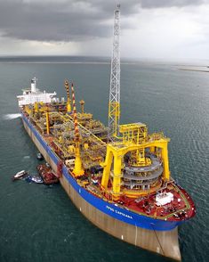 an oil tanker ship in the middle of the ocean under a cloudy sky with cranes on it