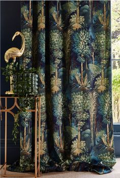 the curtains in this room are blue with green and gold foliage on them, along with a golden flamingo statue