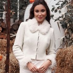 a woman standing in front of hay bales wearing a white coat with fur collar