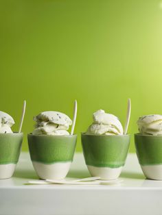 four bowls filled with ice cream on top of a white table next to a green wall