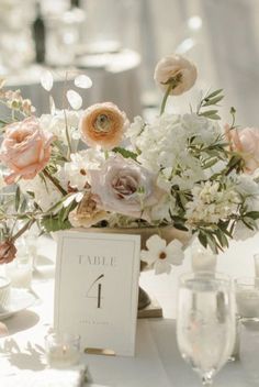 an arrangement of flowers in a vase on top of a white table cloth covered table