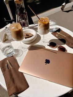 an apple laptop sitting on top of a white table next to glasses and drinks in front of it