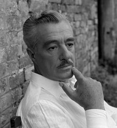 black and white photograph of a man leaning against a brick wall with his finger in his mouth