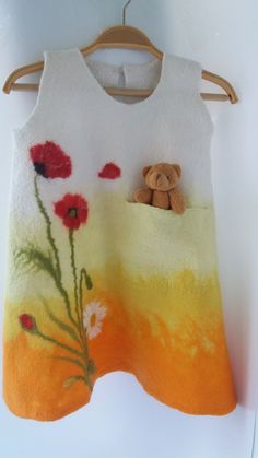 an orange and yellow sweater with a teddy bear in the pocket on a hanger