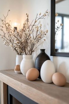 three vases with flowers and eggs sit on a mantle in front of a mirror